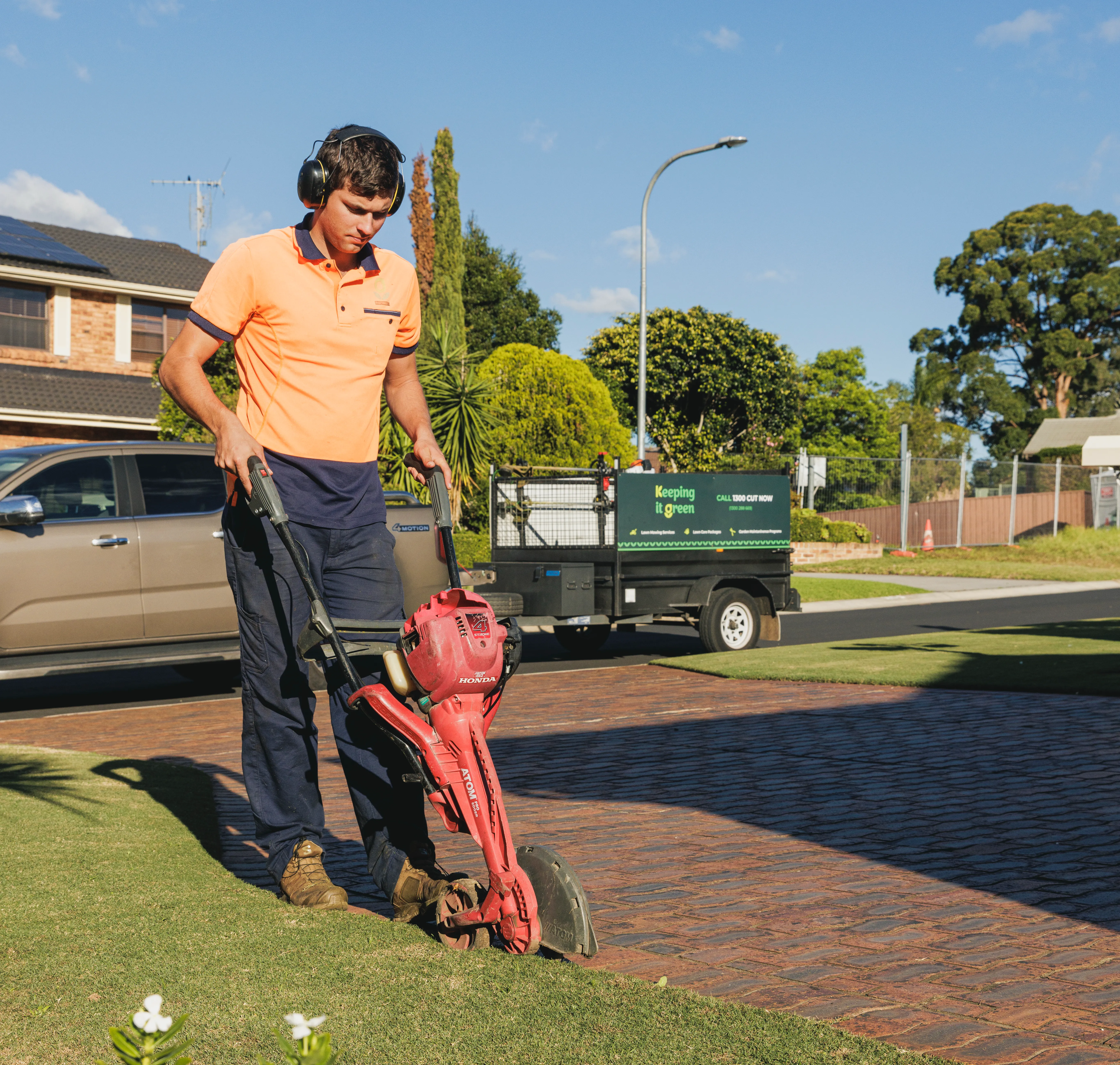 Keeping It Green team member edging a lawn along a brick driveway with an Atom edger