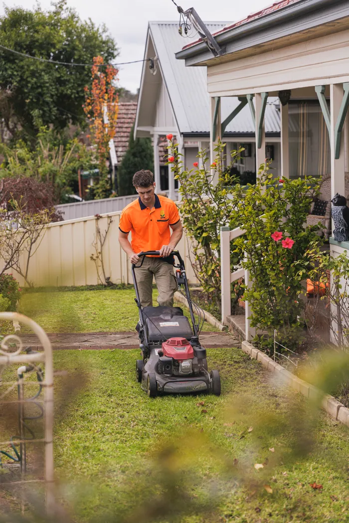 Keeping It Green team member mowing a lawn beside an established Narellan home
